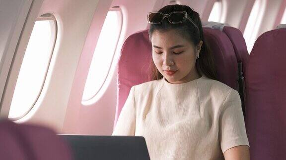 旅游和科技坐头等舱年轻漂亮的女商人坐在飞机上用笔记本电脑工作