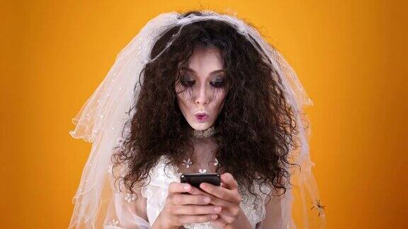 万圣节快乐死去的新娘穿着婚纱用智能手机化妆