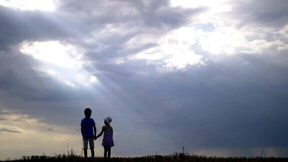 傍晚男孩和女孩手牵着手在云彩的背景下散步