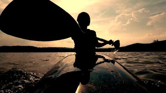 日落时分女子在平静的湖面上划皮艇