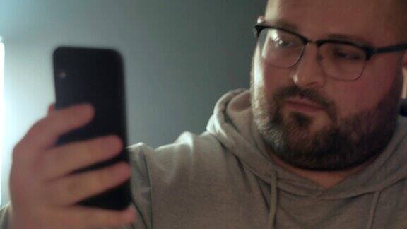 戴眼镜的搞笑胖男人用智能手机微笑着和朋友聊天现代互联网通信技术