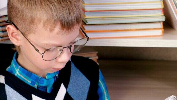 一个七岁的戴眼镜的小男孩坐在书堆里的速写本上画着什么特写镜头的脸