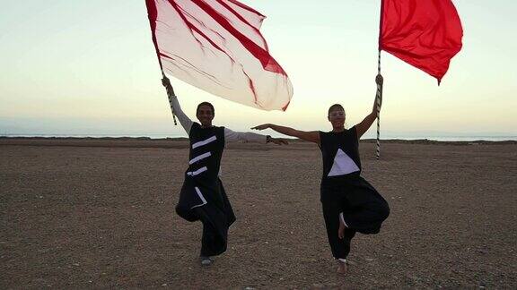 日落时分在摇晃的镜头中两个人拿着红旗在沙漠中表演