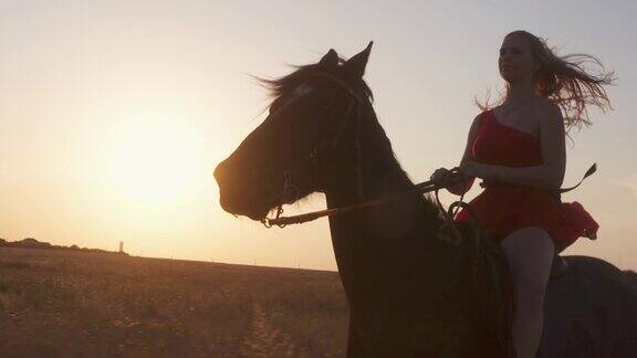 年轻的女孩穿着红色的长裙骑着黑马背对着太阳