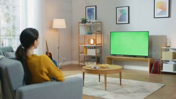 女孩坐在家里的沙发上看着电视绿幕