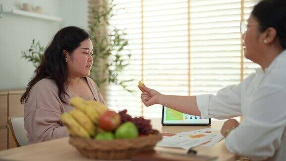 一位亚洲成年人正拿起一颗葡萄给一位身材高大的女士品尝同时向她解释葡萄的营养成分和保健作用