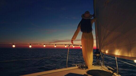 黄昏时分身着长裙的女子在帆船上伸开手臂感受微风