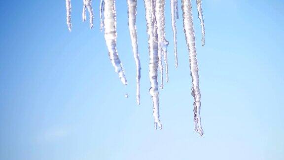 冬天结霜多雪阳光明媚特写镜头巨大的透明冰柱悬挂在屋顶上映衬着天空