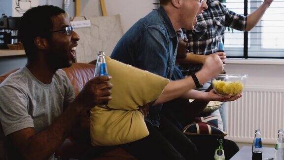 非洲裔美国人朋友看电视上的体育节目缓慢的运动球迷们坐在沙发上吃着爆米花兴奋地庆祝进球情感