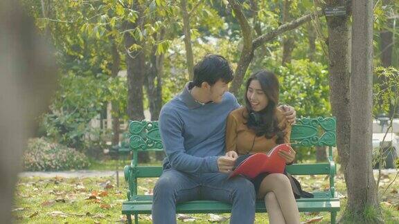 一对快乐的年轻夫妇坐在公园的长椅上一起看书