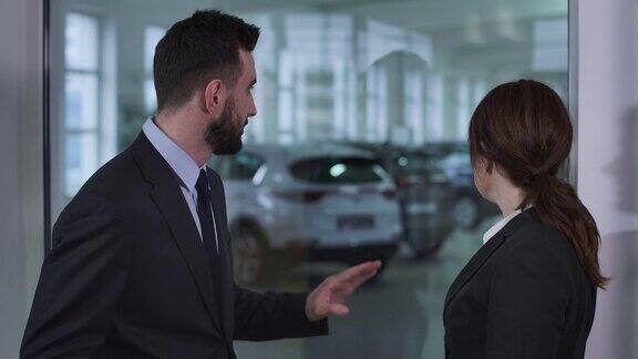 侧视图严肃的白人男人和女人站在汽车经销商和交谈男经销商向女客户解释汽车规格电影4kProRes总部