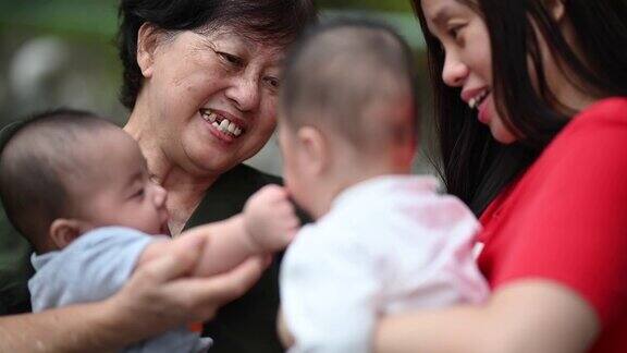 一位年长的亚洲华人妇女和她的双胞胎儿子孙子在他们家的前院和她的女儿一起玩