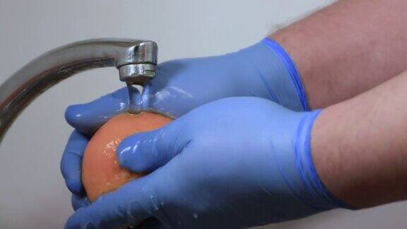 男性双手在手套近处用肥皂和水清洗橘子