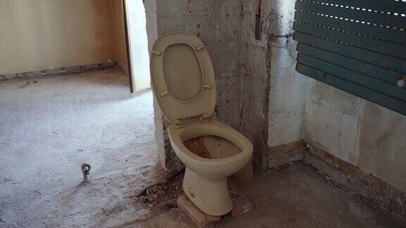 旧的生锈的肮脏的黄色厕所在废弃的房子陶瓷堵塞的厕所倾斜到剥皮的墙壁室内拍摄的被毁的公寓被毁的浴室和肮脏不卫生的厕所修复损坏的建筑结构