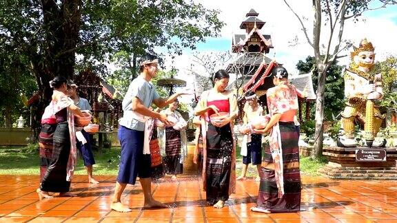 慢动作:美丽的女人穿着传统的泰国服装泼水的男人在寺庙-泼水节