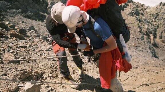 在山上攀爬一段困难的陡坡时教练将下降器连接到攀登者的确保绳