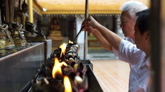 亚洲长者在做佛教仪式为佛像倒油加烛焰