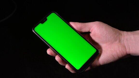 男性手持黑色手机黑色背景下的绿色屏幕