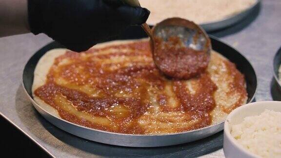 披萨厨师正在用金属勺将番茄酱涂在披萨面团上