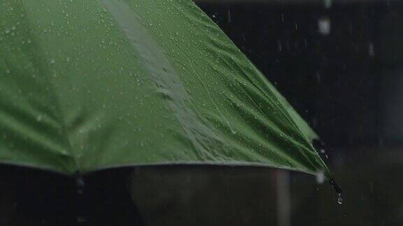 绿色雨伞上的雨滴在黑暗背景下的慢动作镜头