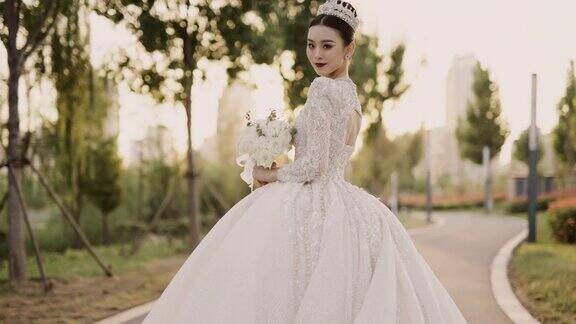 年轻美丽的亚洲新娘穿着白色婚纱漫步在花园中从后面拍摄慢动作