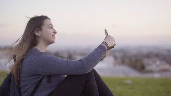 微笑的女人坐在公园里用智能手机自拍