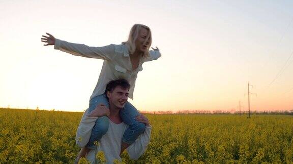 幸福的年轻夫妇有乐趣在黄色的油菜花田在日落