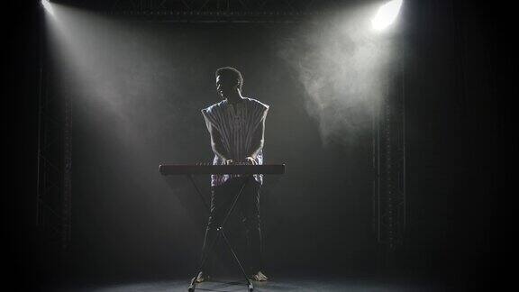 在黑暗的演播室里美国黑人在舞台上弹奏钢琴合成器键盘的剪影一个音乐家画着非洲民族风格的脸在灯光的背景下表演慢动作