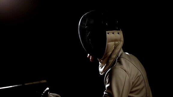 一个男人的特写镜头戴着一个头盔的击剑格斗与一个对手在一个黑暗的背景与剑工作室拍摄