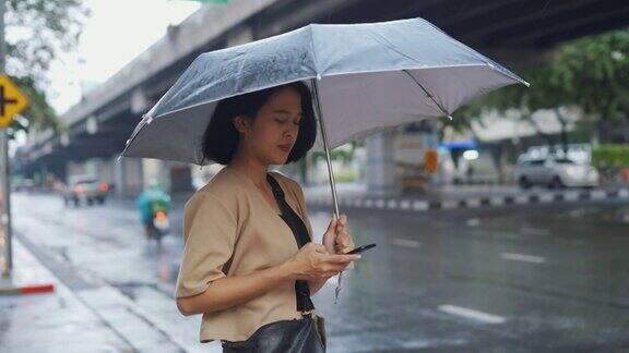 亚洲女子在雨中等出租车时使用手机