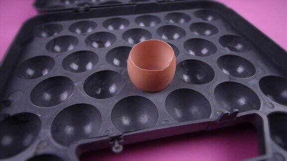 在粉红色背景的灰色托盘中空的碎蛋壳