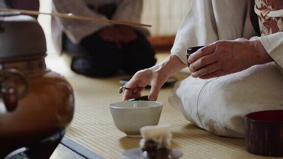 茶道主持人将茶叶从茶叶罐中舀入碗中客人在一旁观看