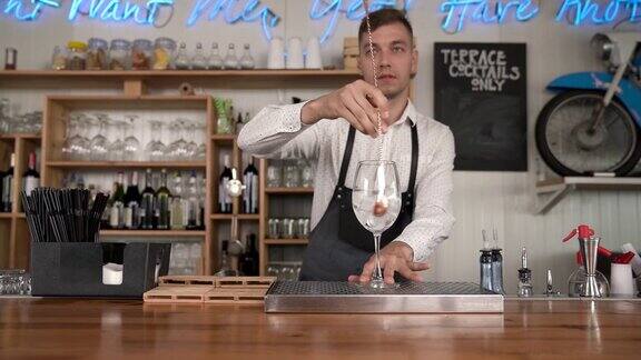 酒保将冰块倒入玻璃杯一个年轻英俊的酒保用酒吧勺子把冰倒进玻璃杯