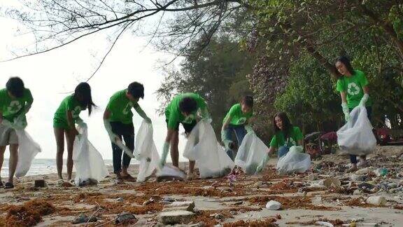 一群穿着绿色t恤的亚洲年轻人志愿者用装满垃圾的塑料袋清理海滩生态安全概念4k决议