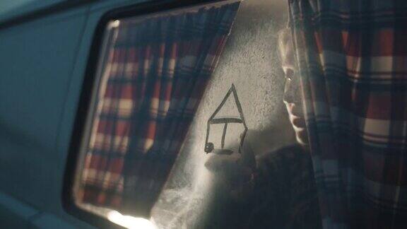 一个女人在露营车雾蒙蒙的窗户玻璃上画房子