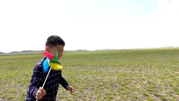 一个亚洲男孩在草原上和风车赛跑