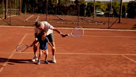 骄傲的爷爷教他的孙子打网球
