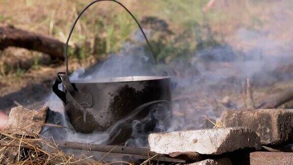 日落时分在烟雾中的篝火上用平底锅烹饪食物4K