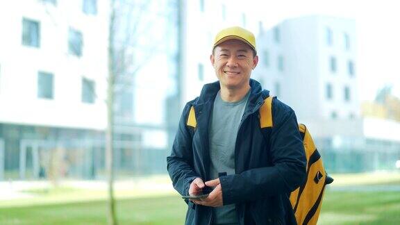 亚洲快乐男性快递服务人员的肖像戴着帽子背着背包城市街道上的员工在城市背景下看着镜头微笑