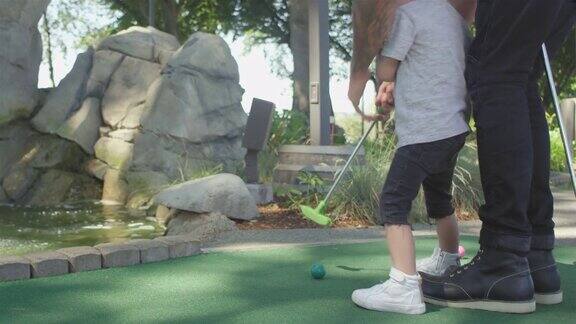 一个小孩在高尔夫球场上奋力击球他的妈妈帮助他和球