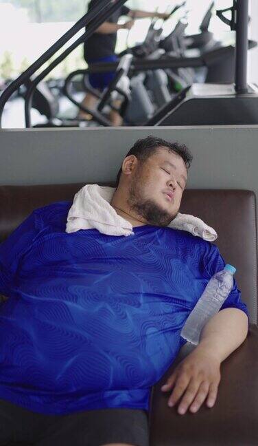 疲惫的肥胖男子在健身房锻炼后躺在沙发上睡觉