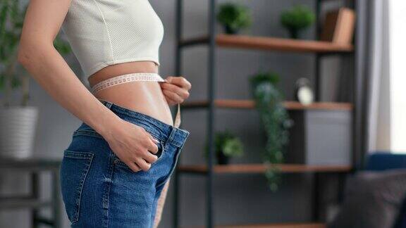 特写无法辨认的苗条女人在超大的大牛仔裤测量腰围减肥吸脂