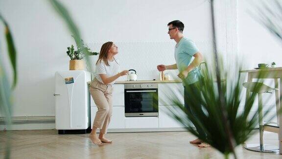 年轻的女孩和男孩有乐趣在厨房在家里一起跳舞大笑
