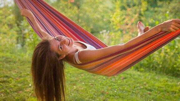 快乐的年轻女子在后院树下的吊床上荡秋千对着镜头笑着玩