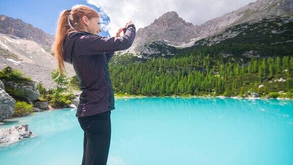 一名女子在山湖上欣赏风景用智能手机拍照背景是山脉