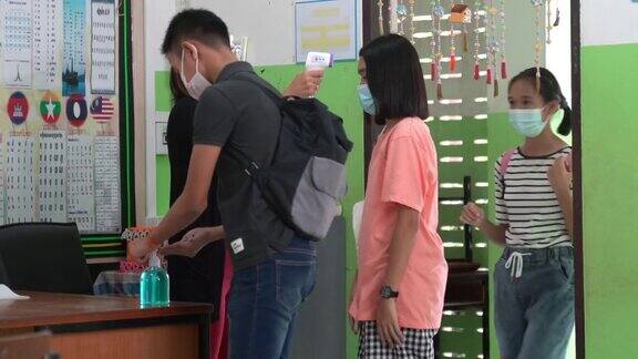 年轻老师用体温计检查亚洲小学生戴口罩防止病毒在进入教室前再次开始上课
