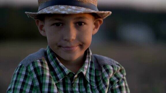 一个戴着草帽的乡村男孩在日落时看着摄像机的肖像