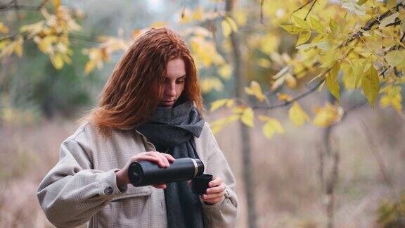 在秋天的森林里一位红发美女正在用保温瓶喝茶