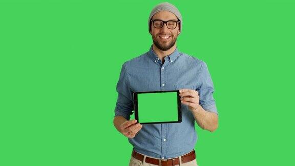 一个微笑的年轻人戴着眼镜展示绿色屏幕的平板电脑的中景背景中的绿色屏幕