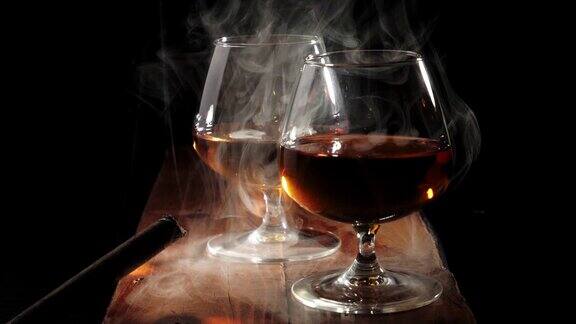 豪华白兰地棕色的木桌上放着两杯金色的干邑和冒烟的雪茄背景是黑色冒烟了白兰地干邑嗅酒狂欢